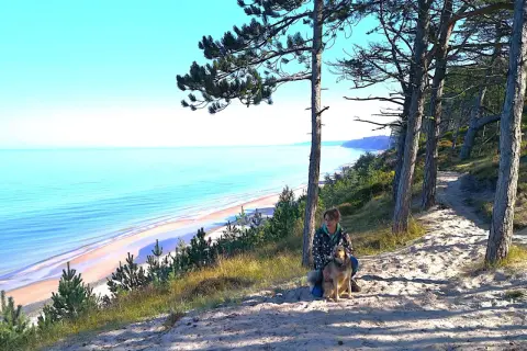 Frau mit Hund auf einem sandigen Pfad mit Blick auf die polnische Ostsee.