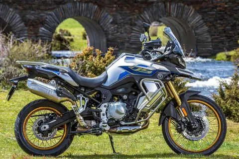 Moto Voge 500DS, una moto china con motor BMW, lista para la aventura junto a un puente de piedra y un río.