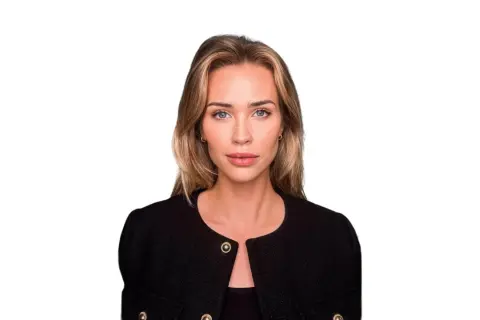 Isabella Jedler, en kvinna med blont hår och blå ögon, bär en svart kavaj med gulddetaljer.