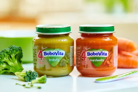 Dwa słoiczki BoboVita: brokuły i marchewka, idealne jako pierwsze pokarmy dla niemowląt po 4 miesiącu. Obok świeże warzywa.