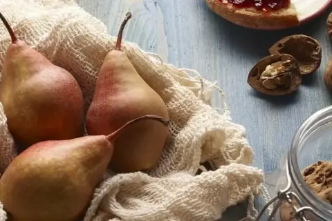 Trzy rumiane gruszki na białym materiale, obok orzechy i słoik z ciasteczkami. Czy gruszki są zdrowe? Tak, to pyszny i zdrowy owoc!