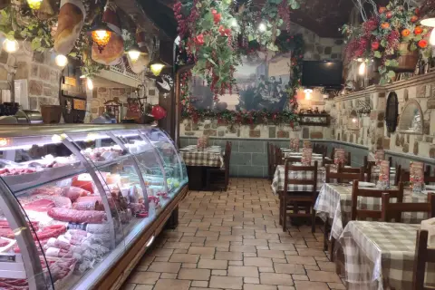 Wnętrze restauracji w stylu rustykalnym, z wiszącymi wędlinami i dekoracjami. W chłodni mnóstwo wyrobów, jak w najlepszym sklepie w Frascati.