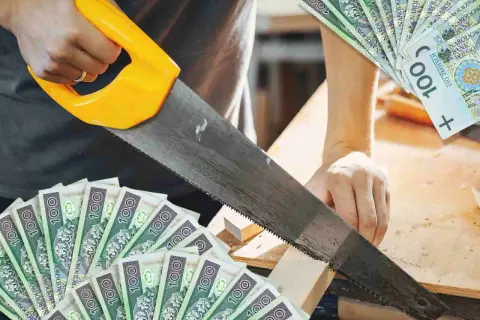 Cieśla tnie drewno piłą, a wokół leżą banknoty 100 zł. Zarobek rzemieślnika.