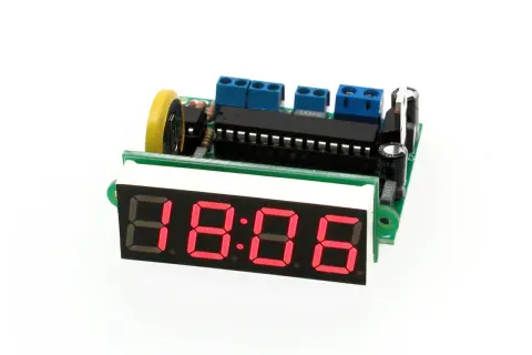 Elektroniczny zegar z czerwonym wyświetlaczem 18:06, zasilany przez płytkę drukowaną z elementami, w tym oscylatorem.