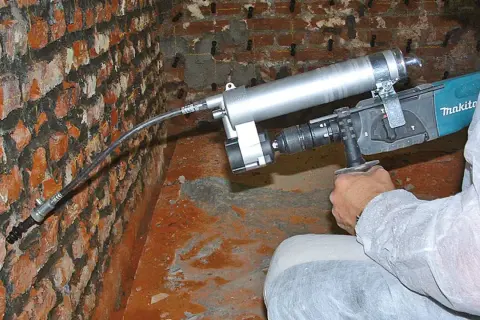 Gerät zur nachträglichen **Verkieselung Mauerwerk selber machen**. Ein Mann injiziert eine Flüssigkeit in eine Ziegelwand.