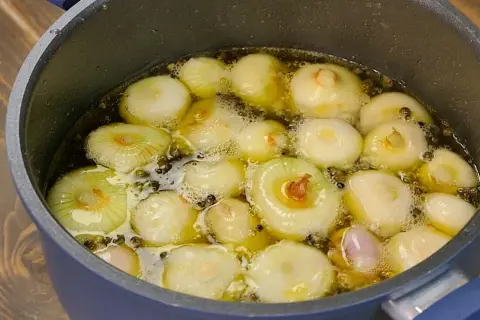 Cipolline in agrodolce in padella con aceto balsamico, che sobbollono in un liquido dorato, pronte per essere gustate.