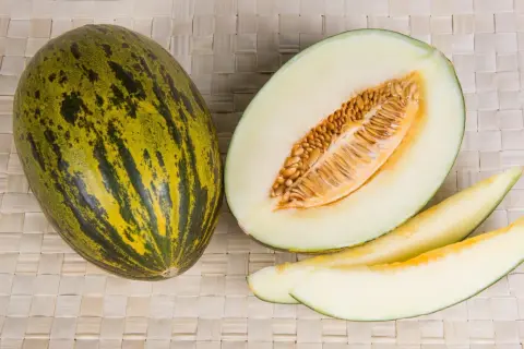 Un intero melone di Borgogna, tagliato a metà e a fette, mostra la sua polpa chiara e i semi dorati.