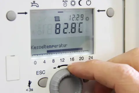 Hand stellt die vorlauftemperatur gasheizung ein. Kesseltemperatur 82.8°C.