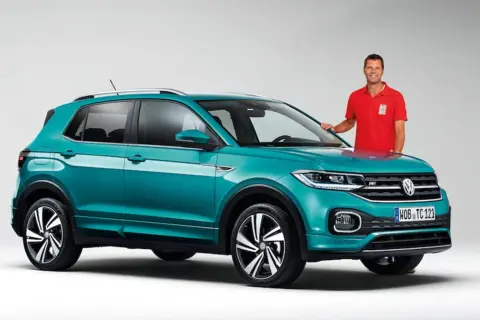 Mężczyzna w czerwonej koszulce stoi obok turkusowego Volkswagena T-Cross, który przekracza wymiary miejskiego auta.