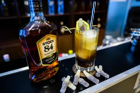 Butelka brandy Stock 84 i drink z cytryną, słomką i żelkami w kształcie butelek.