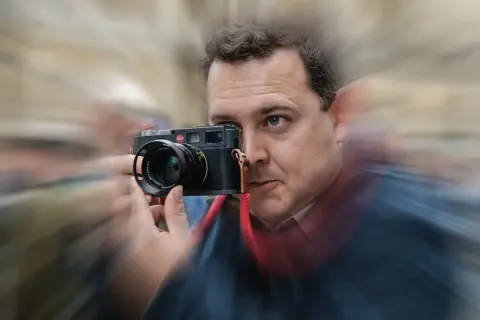 Man with Leica camera, possibly contemplating the best focal length for street photography.