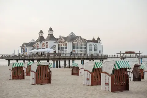 Plaża w Stralsundzie w Niemczech z charakterystycznymi koszami plażowymi i molo z białą budowlą.