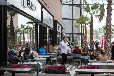 Gente disfrutando en los restaurantes de la torre outlet, rodeados de palmeras y flores.