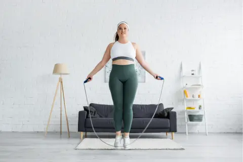 Eine Frau springt mit einem Seil in einem hellen Wohnzimmer. Sie fragt sich, wie oft Sport in der Woche gut ist.