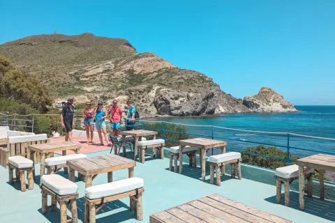 Terraza del cala higuera restaurante con mesas de madera y vistas al mar. Un grupo de amigos disfruta del sol.