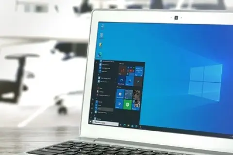 Laptop z systemem Windows 10 LTSC na biurku, w tle biuro z krzesłami.