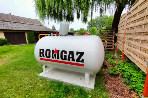 Biały zbiornik na gaz ziemny z napisem ROMGAZ, podłączony do instalacji ogrzewania gazowego z butli.