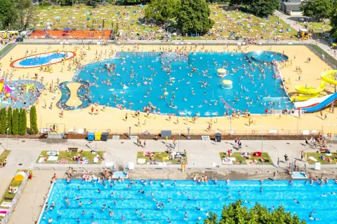 Tłum ludzi cieszy się słońcem i wodą w moczydło water park. W basenach i na trawie panuje wakacyjna atmosfera.