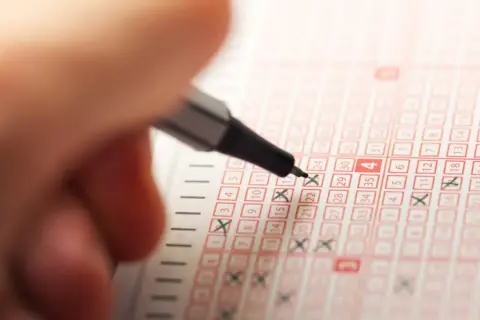 Dłoń z długopisem zaznacza liczby na kuponie Lotto.
