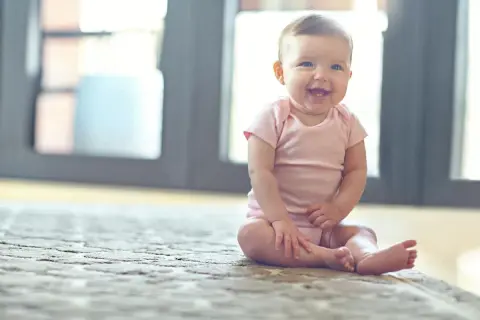 Ein fröhliches Baby sitzt auf einem Teppich und lacht.