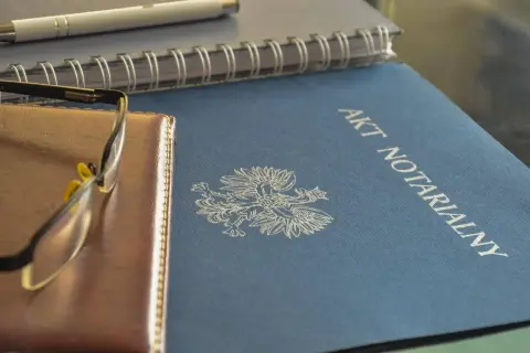 Akt notarialny z orłem, obok notes i okulary. To ważne dokumenty, tworzące repertorium prawnicze.