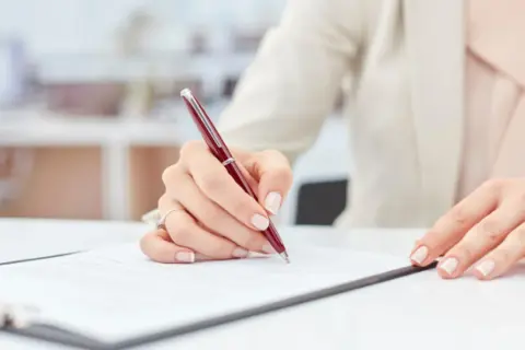 Dłoń podpisuje ważny dokument, być może weksel, na białym biurku.