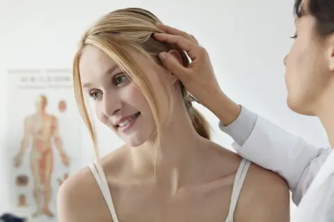 Lekarz bada skórę głowy pacjentki. Czy potrzebuje skierowania do dermatologa?