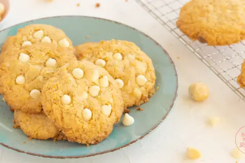 Saftige white chocolate macadamia cookies auf einem türkisfarbenen Teller, daneben Macadamianüsse und Schokostückchen.