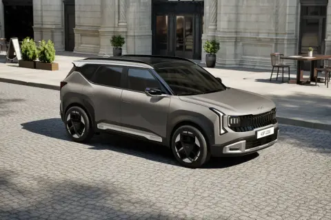 Nowoczesne kia modele, jak ten szary SUV, prezentują się stylowo na brukowanej ulicy przed kawiarnią.