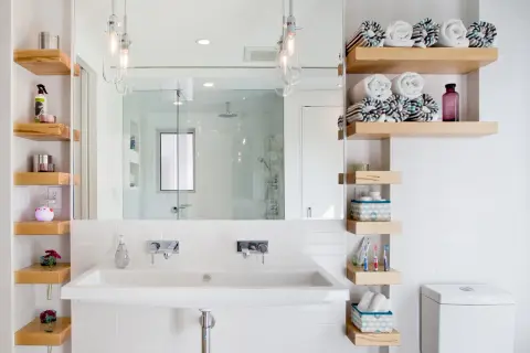 Étagères flottantes en bois pour une astuce rangement petite salle de bain. Serviettes roulées, produits de toilette et décorations y trouvent leur place.
