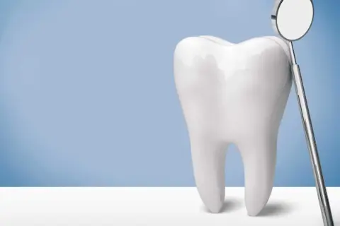 Biały ząb obok lusterka dentystycznego. Po piaskowaniu zębów uśmiech jest olśniewający.