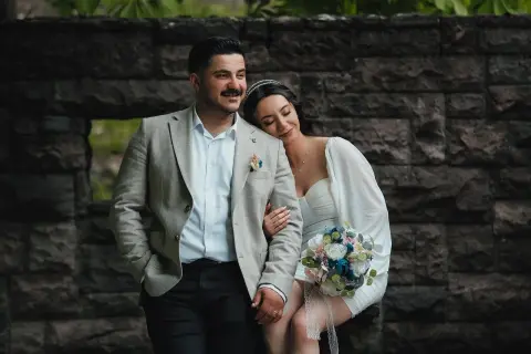 Para młoda w stylizacjach ślubnych na tle kamiennej ściany.
