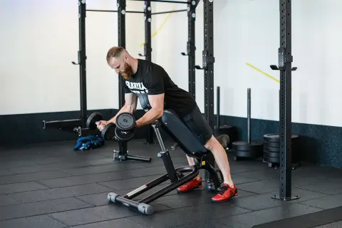 Mężczyzna wykonuje ćwiczenie incline dumbbell curl na ławce skośnej, budując masę mięśniową ramion.