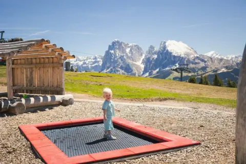 Mały chłopiec cieszy się zabawą na trampolinie na tle majestatycznych Dolomitów.
