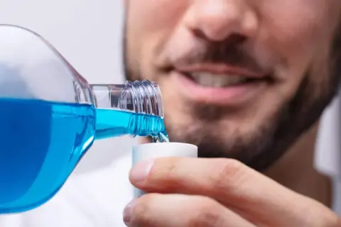 Hombre sonriente vierte clorhexidina diluida en un vasito dosificador para su higiene bucal.