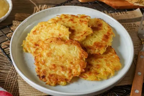 Goldbraune, knusprige Kartoffelpuffer aus gekochten Kartoffeln liegen auf einem Teller. Dazu passt Apfelmus.