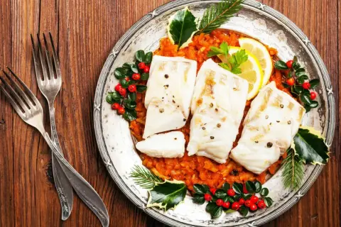 Gedünsteter Fisch auf Tomatenragout, festlich dekoriert mit Beeren und Tannenzweigen. Ein Gericht, das an italienische Weihnachtsrezepte erinnert.