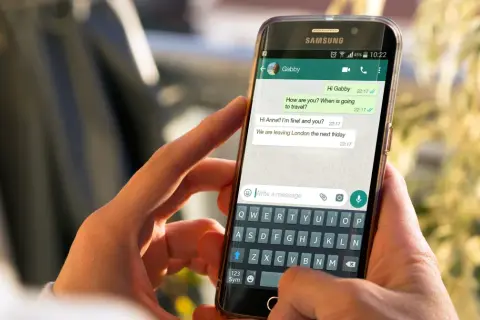 Dłonie trzymają smartfon z otwartym WhatsAppem. Widoczna jest rozmowa i klawiatura, co może pomóc w nauce jak zainstalować WhatsApp.