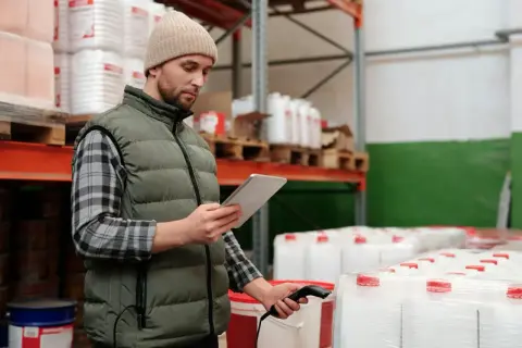 Pracownik magazynu sprawdza stany magazynowe, skanując produkty tabletem.
