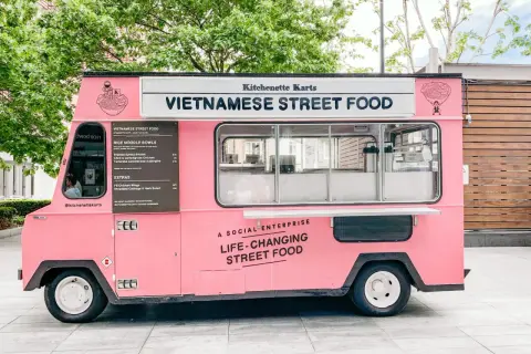 Un food truck rosa brillante, "Kitchenette Karts", offre "Vietnamese Street Food" e cibo che cambia la vita.
