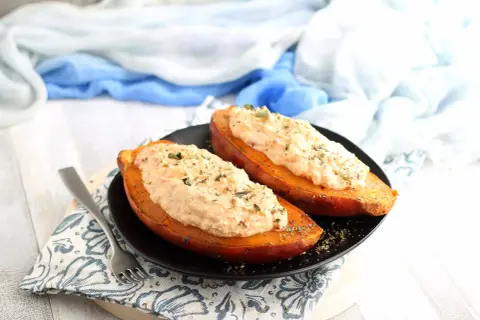 Due patate dolci al forno, tagliate a metà e farcite con un cremoso ripieno, guarnite con erbe aromatiche.