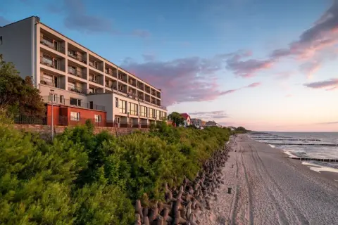 Idealne noclegi przy plaży z widokiem na morze. Hotel z balkonami wychodzącymi na piaszczystą plażę i spokojne morze o zachodzie słońca.