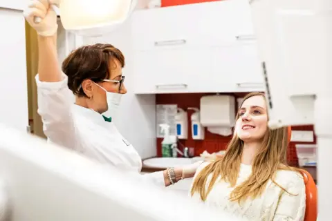 Dentystka przygotowuje się do chirurgicznego usuwania ósemki w ciąży. Pacjentka uśmiecha się, ufając profesjonalistce.