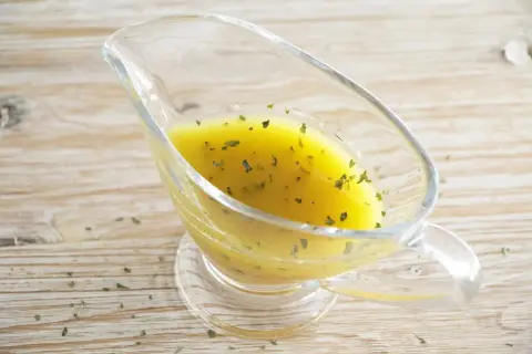 Salsa dorada con hierbas verdes en una salsera de cristal. Perfecta vinagreta de mostaza para realzar tus platos.