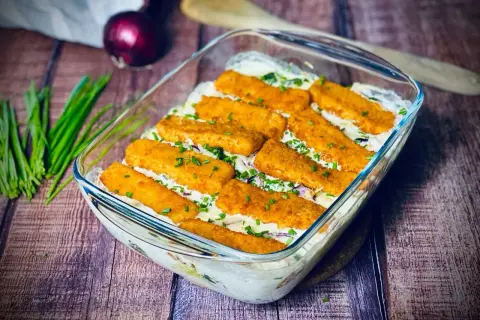 Ausgefallene Gerichte: Fischstäbchen-Auflauf mit cremiger Soße und frischen Kräutern, garniert mit Schnittlauch.
