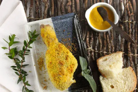 Fusi di pollo al forno dorati e croccanti, serviti con pane fresco, salsa gialla e rametti verdi.