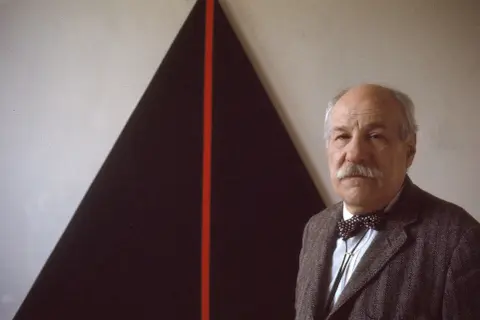 John Plaster poses in front of a striking abstract painting, possibly at the Guggenheim.