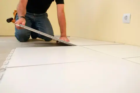Hombre colocando baldosas blancas, un paso clave para como poner suelo porcelanico.