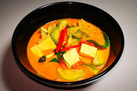 Ein dampfendes rotes Curry mit Tofuwürfeln, grünen Tomaten und scharfen Chilischoten. Dieses rote Curry ist scharf und verlockend.