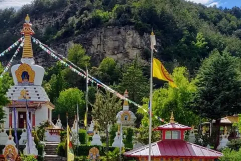 El templo budista Huesca, rodeado de vegetación, con estupas blancas y banderas de oración ondeando.